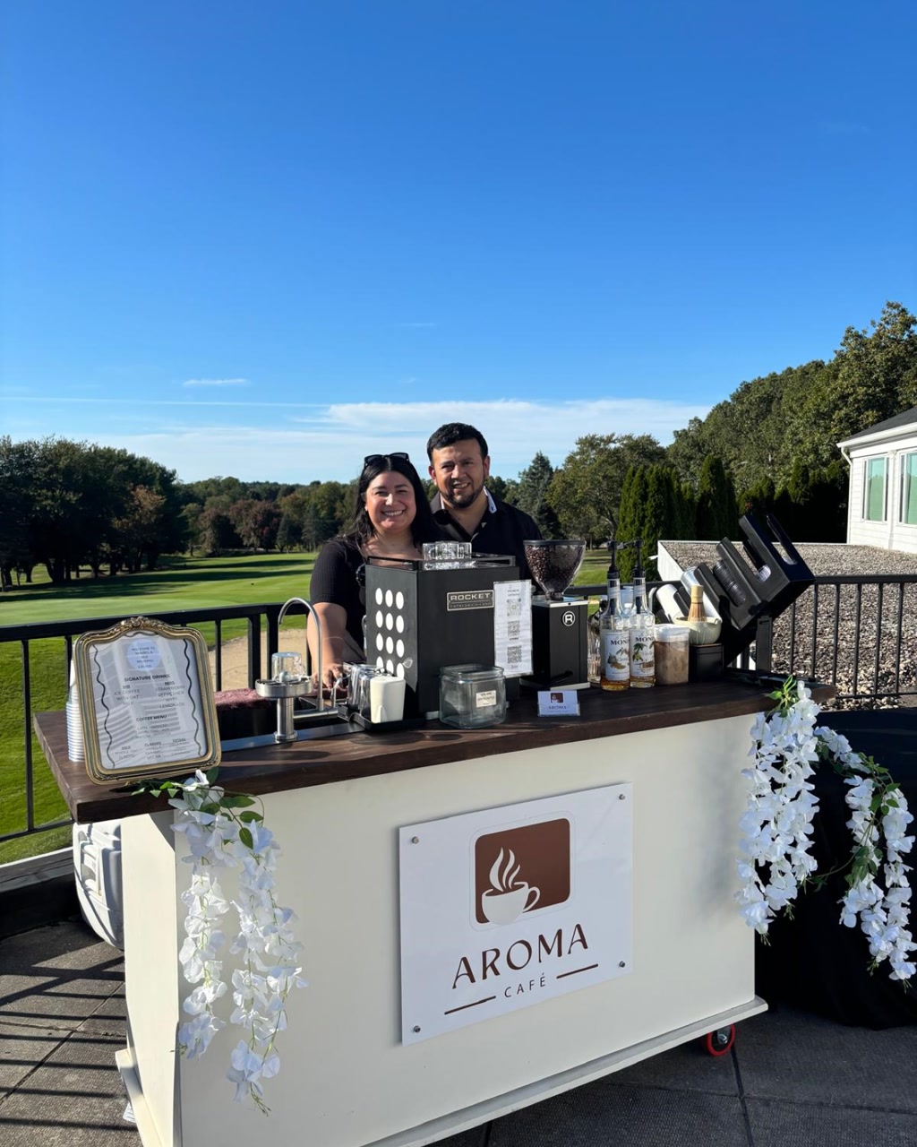 Two baristas behind the Aroma Café cart on a sunny day